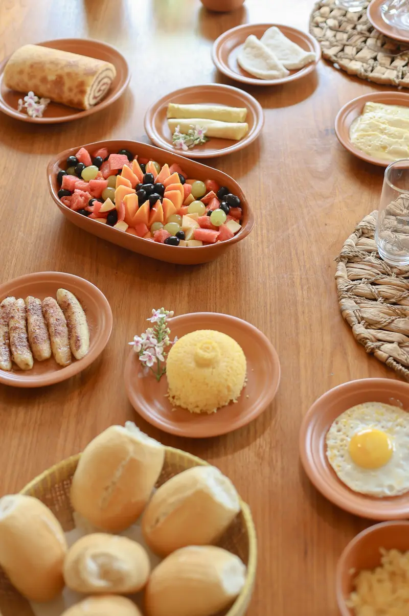 Café da manhã com pães, frutas, cuscuz e ovos em louça de barro