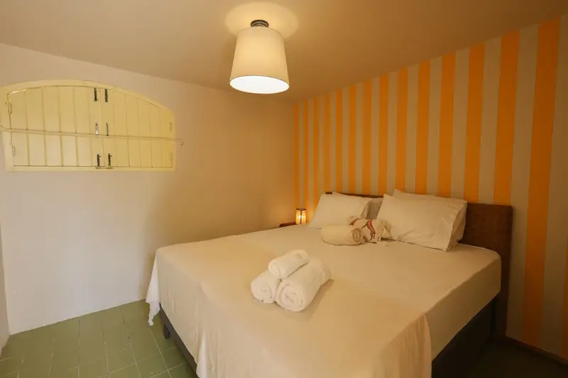 Suíte de apoio, com cama de casal e parede listrada em ocre